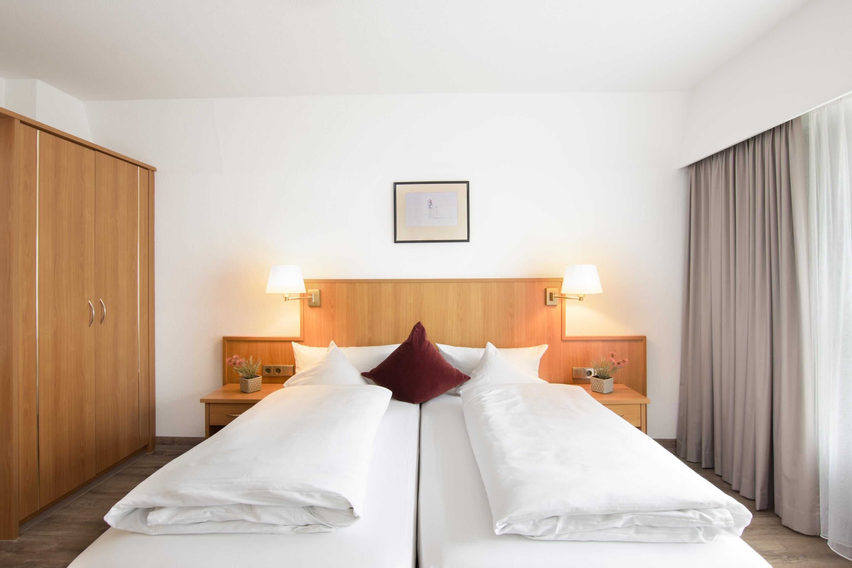 Una habitación de hotel con cama doble, armario de madera, lámparas de noche y un cuadro en la pared.