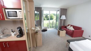 Ein Hotelzimmer mit Küchenzeile, einem Bett, einem roten Sofa, einem kleinen Tisch und Blick ins Freie.