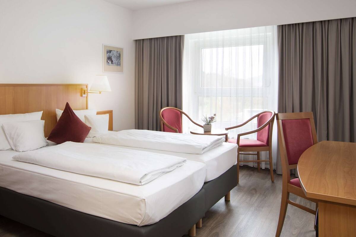 A hotel room with two beds, a desk, a chair, and a window with curtains.