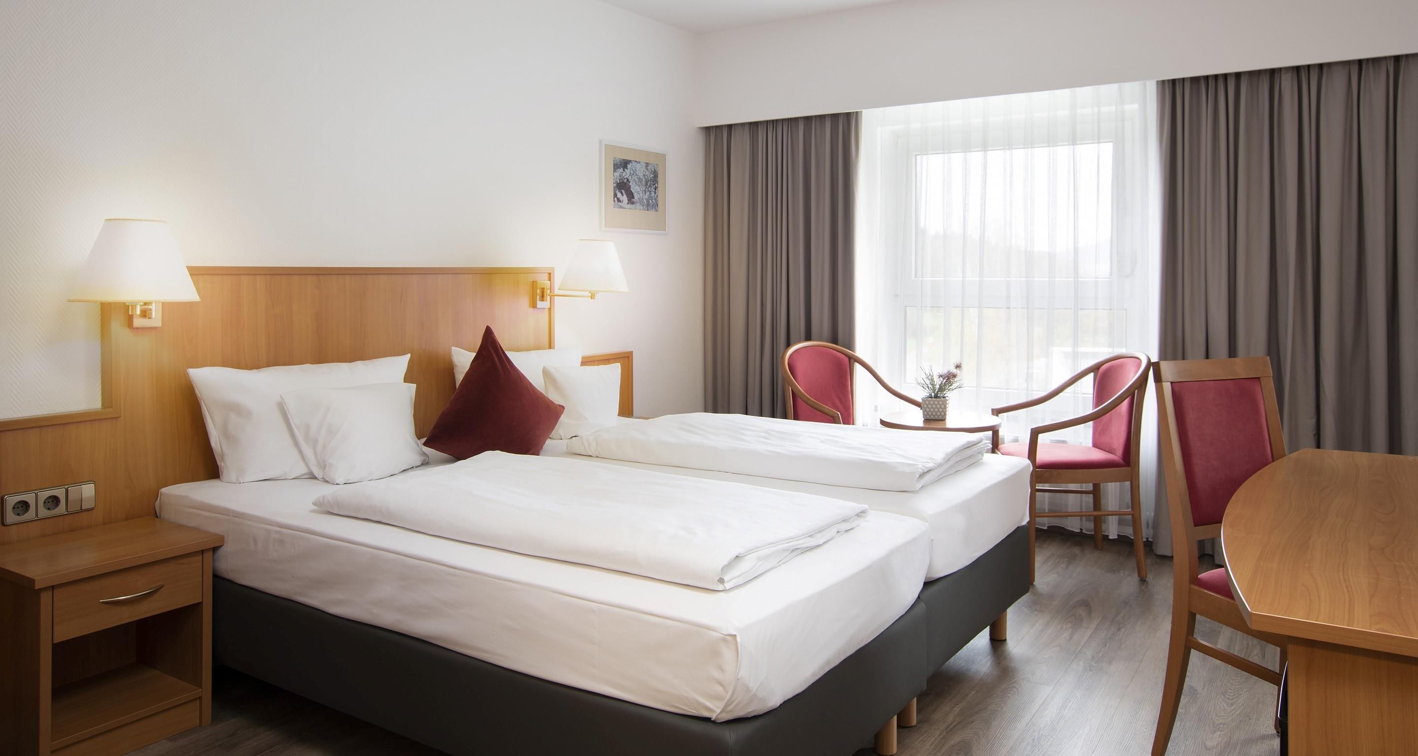 A hotel room with two beds, a desk, a chair, and a window with curtains.