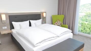 Habitación de hotel con cama, lámparas de noche, una silla verde y vistas al exterior con vegetación.