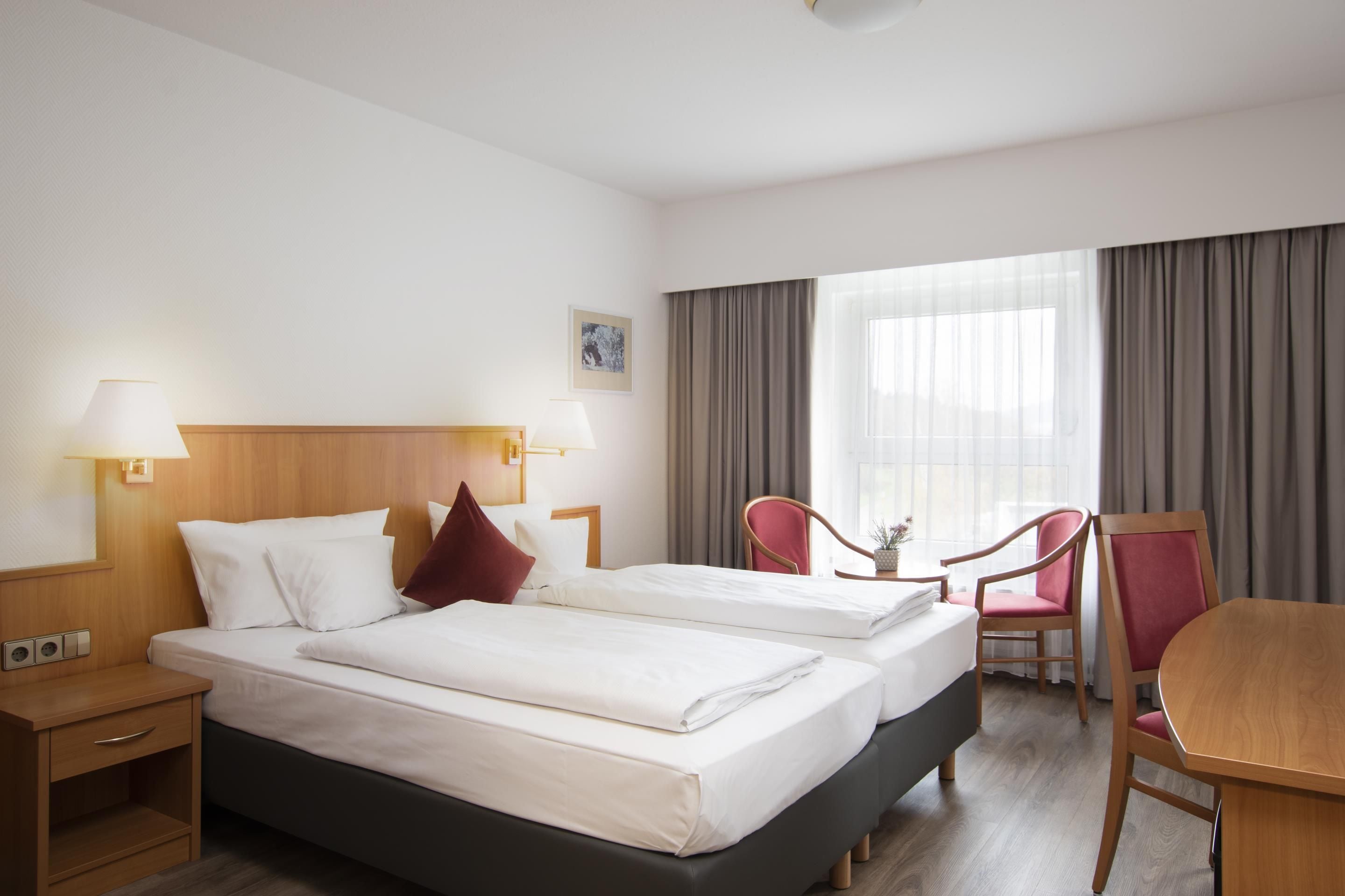 A hotel room with two beds, a desk, a chair, and a window with curtains.