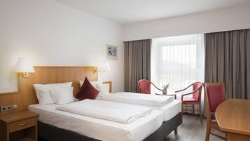 Quarto de hotel com duas camas, uma mesa, uma cadeira e janela com cortinas.