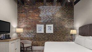 Een hotelkamer met een bakstenen muur, een bed, een stoel, een televisie en twee ingelijste foto's.