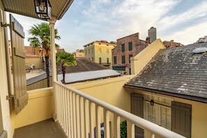 Ein Balkon mit Blick auf umliegende Gebäude, darunter ein Backsteinhaus und ein Gebäude mit grüner Fassade.