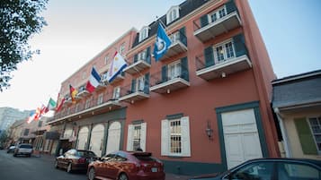 Un edificio con varios balcones y banderas, con una fila de coches aparcados en la parte delantera.