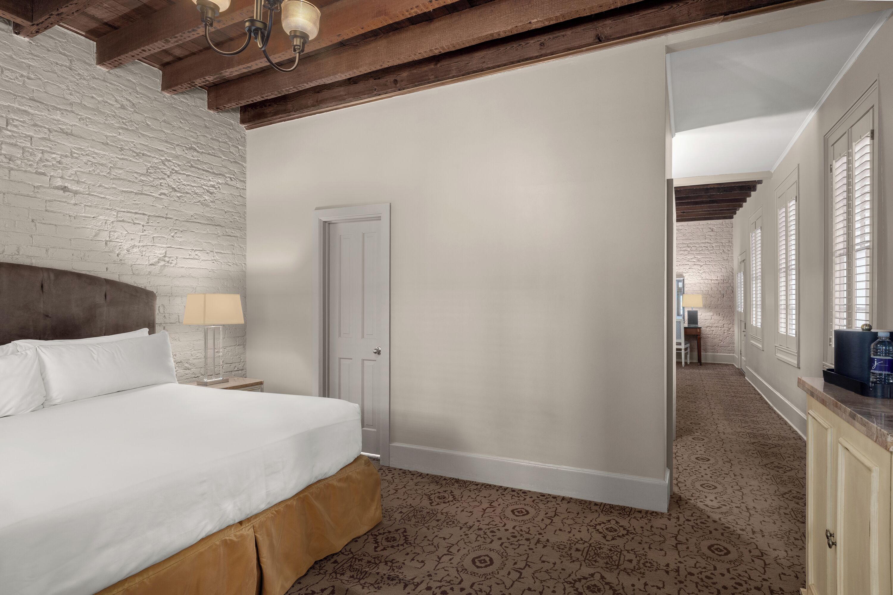 Ein Hotelzimmer mit einem großen Bett, einem hölzernen Kopfteil, einer weißen Tür und einem gemusterten Teppich.