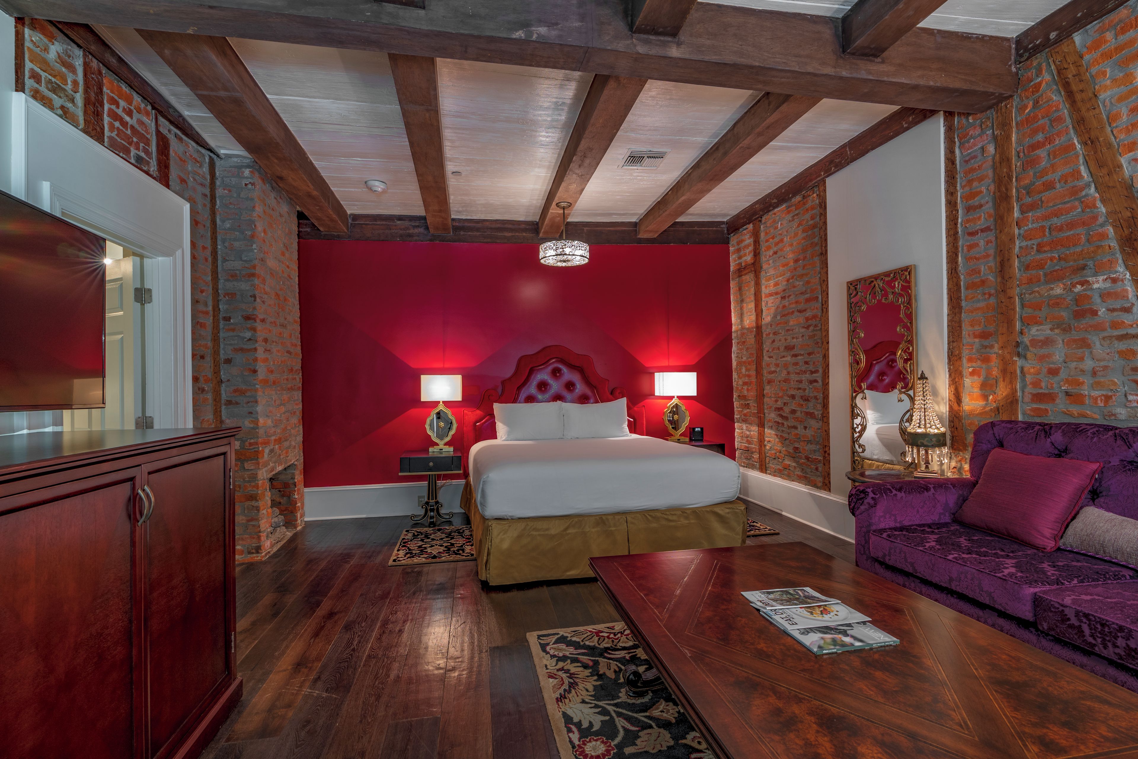 A room with a bed, a sofa, a wooden cabinet, and a red accent wall.