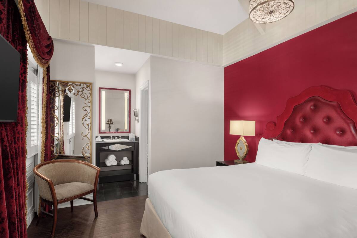Une chambre d’hôtel avec un grand lit, une chaise, une coiffeuse avec un miroir et un mur d’accent de couleur rouge.