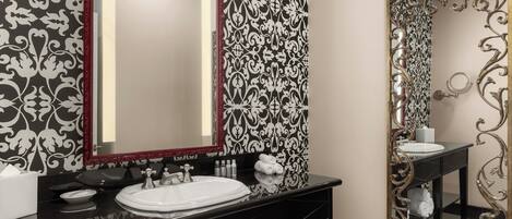 Un baño con tocador negro, lavamanos blanco y dos espejos con marcos ornamentados.