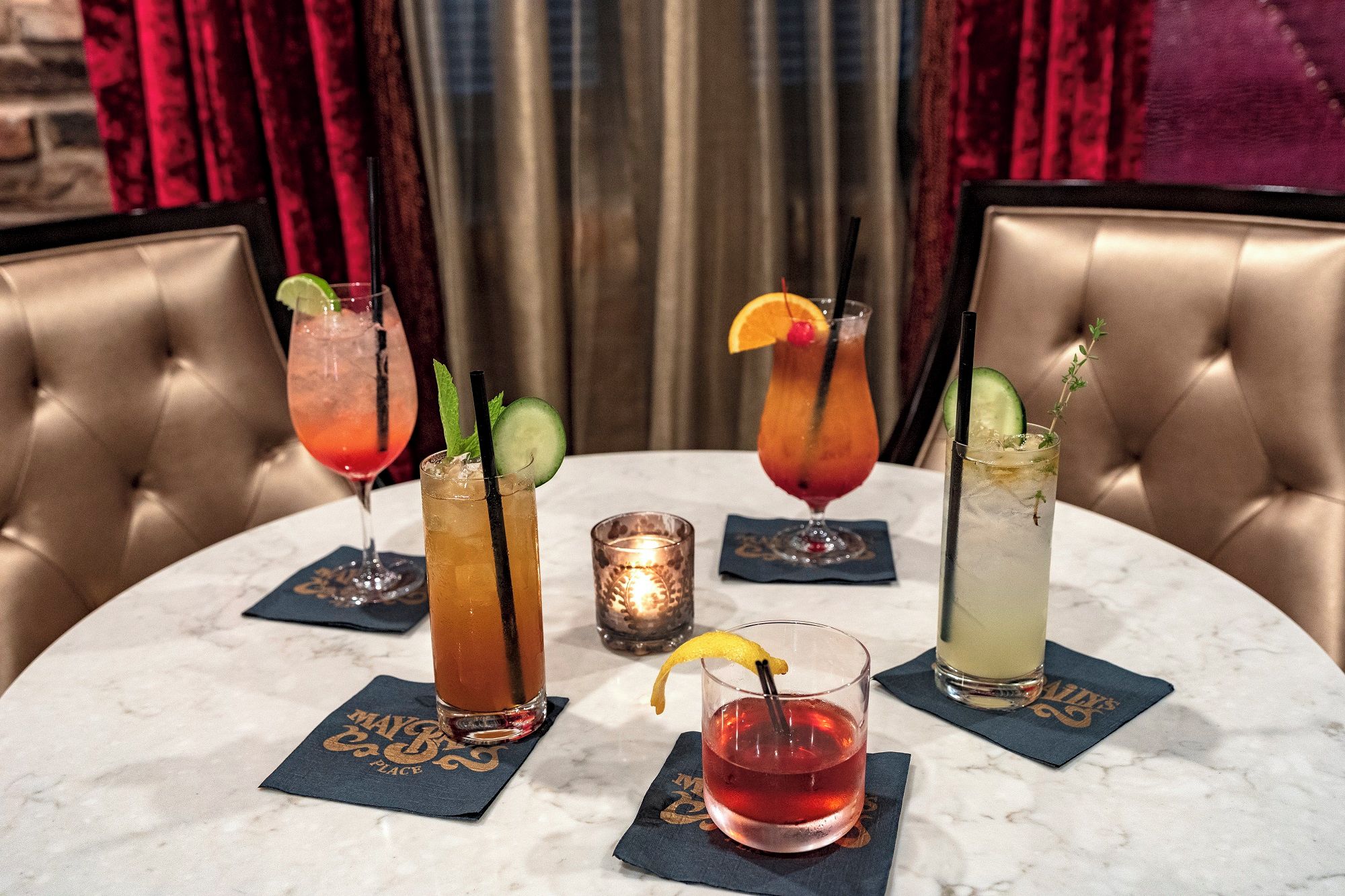 Una mesa con cuatro bebidas, cada una con un adorno diferente, y una vela en el centro.