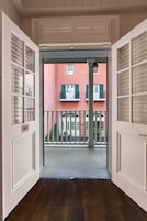Un pasillo interior con vista a un edificio rojo con balcones y contraventanas.