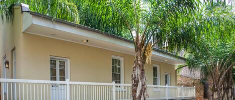 A two-story building with a balcony, surrounded by lush greenery and a small water feature.