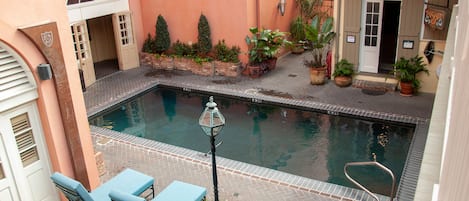 A swimming pool with lounge chairs, surrounded by potted plants and a brick pathway.