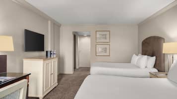A hotel room with two beds, a flat-screen TV, a desk with a lamp, and framed pictures on the wall.