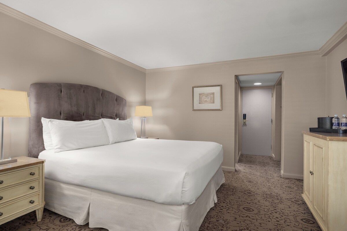 A hotel room with a large bed, two bedside tables with lamps, a wardrobe, and a framed picture on the wall.