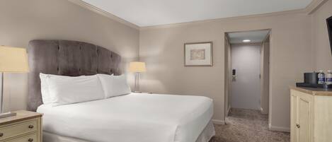 Une chambre d’hôtel avec un grand lit, deux tables de chevet avec des lampes, une armoire et un tableau encadré au mur.