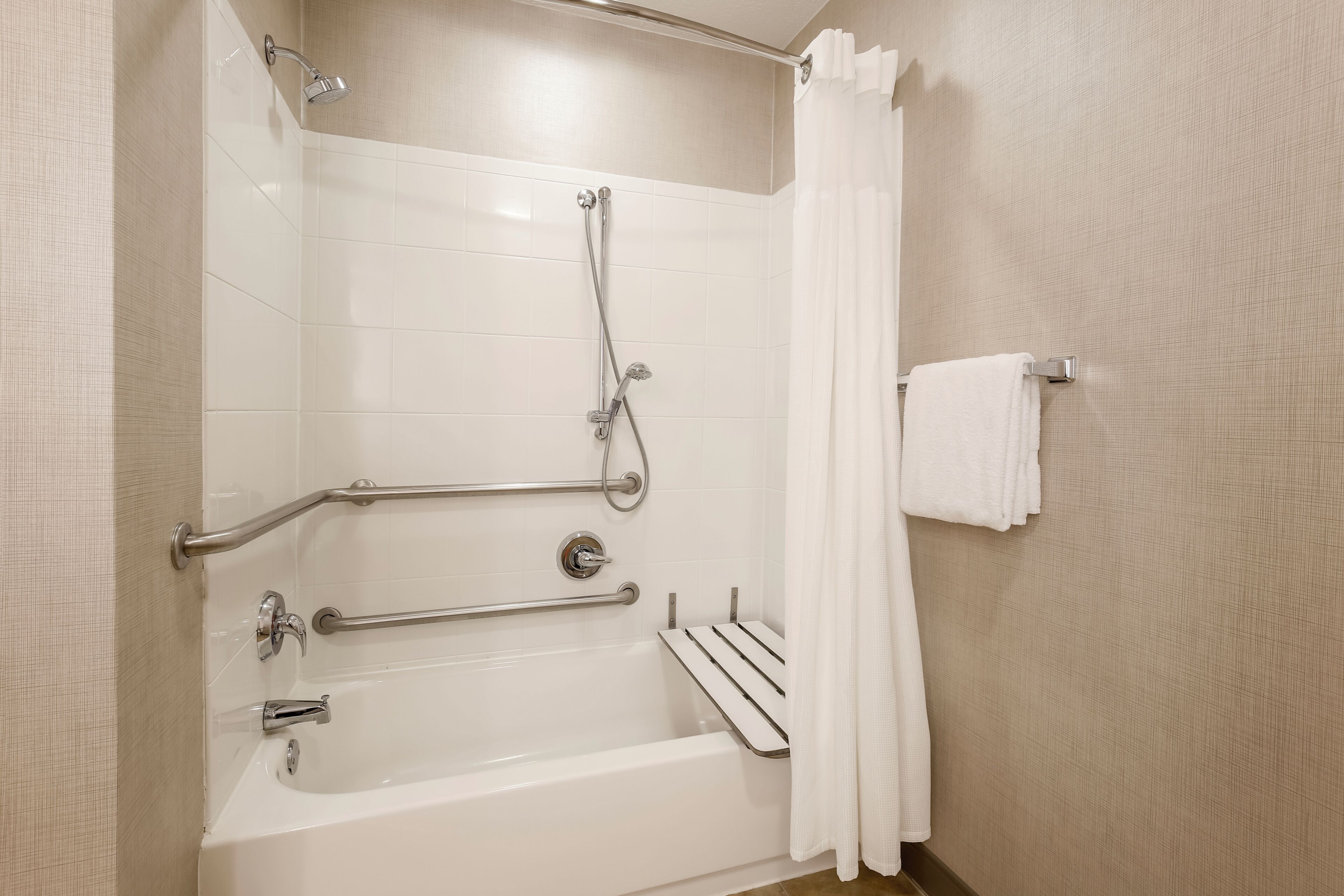 A bathroom with a bathtub, a shower, grab bars, and a towel rack.