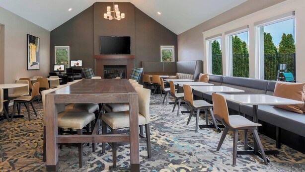A modern dining area with a large wooden table, multiple seating options, and a television mounted above a fireplace. - Residence Inn by Marriott Boston North Shore/Danvers (Danvers)