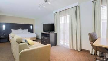 Una camera d'albergo con un letto, un divano, una scrivania, una televisione e tende.