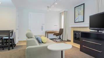 A modern living room with a sofa, a dining table, a TV, and a fireplace.