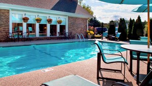 A swimming pool with lounge chairs and umbrellas, a brick building with hanging flower baskets, and a fenced area with outdoor seating. - Residence Inn by Marriott Boston North Shore/Danvers (Danvers)