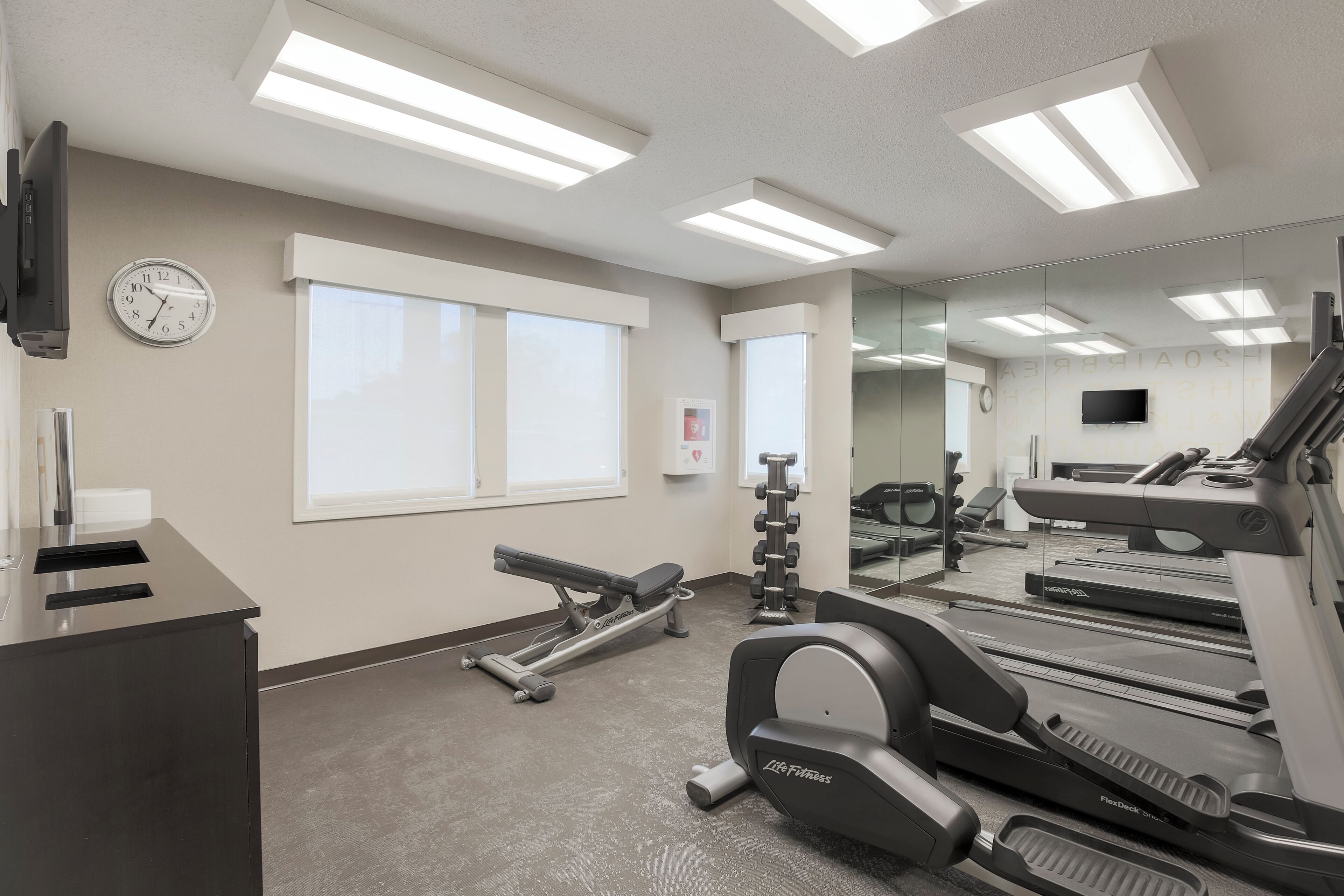 Un gimnasio con cintas de correr, una máquina de remo y un televisor montado en la pared.