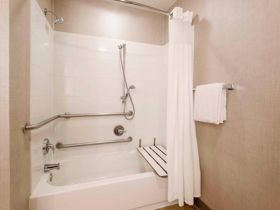Un baño moderno con bañera, ducha, barras de apoyo y un perchero para toallas.