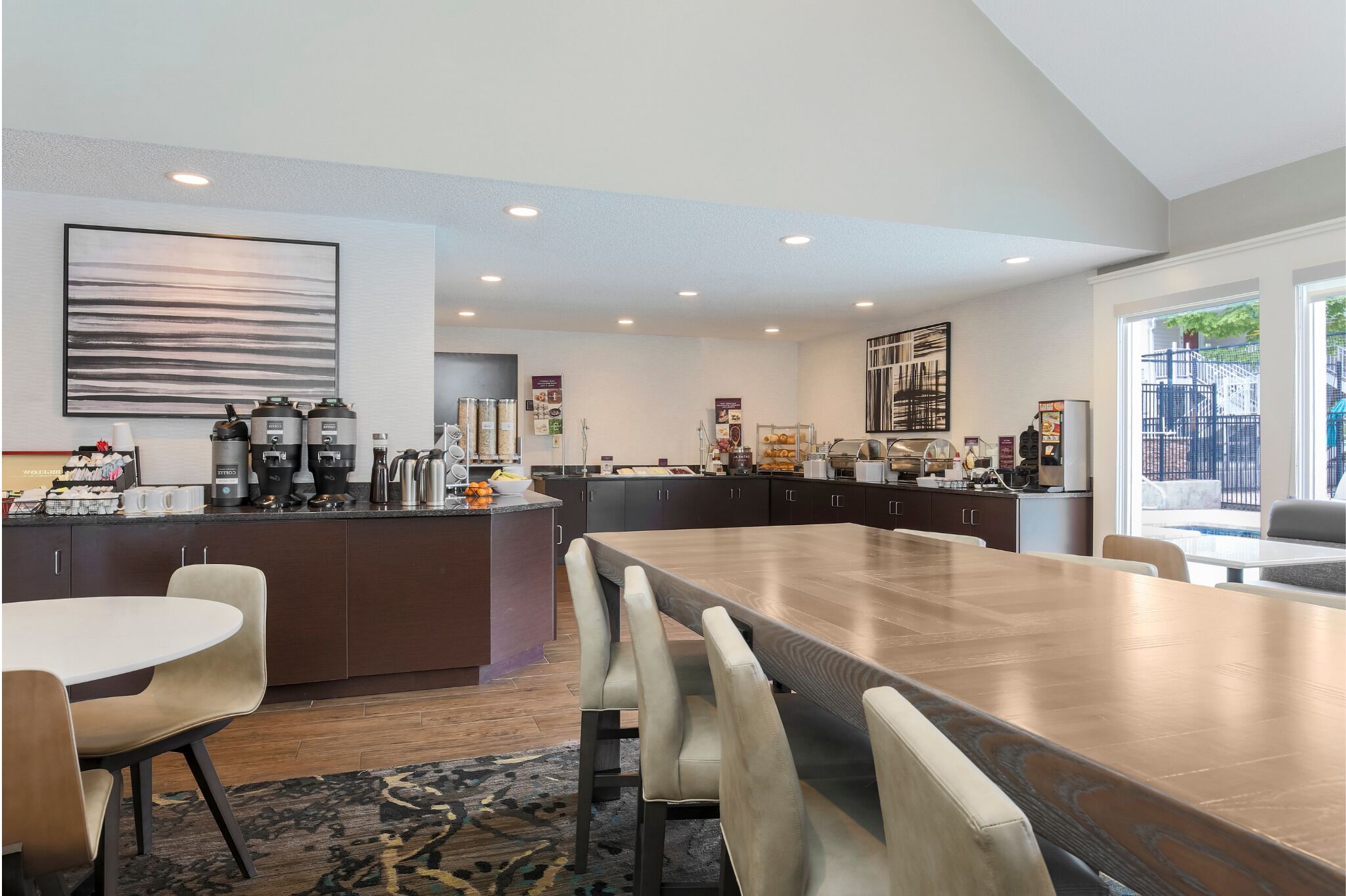 A modern kitchen with a large island, dark cabinetry, and a dining area with a long table and chairs.