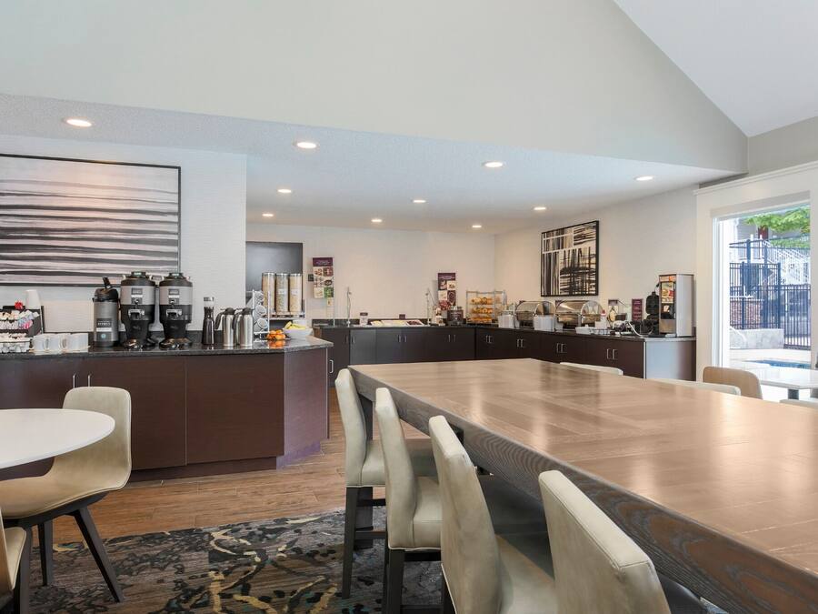 A modern kitchen with a large island, dark cabinetry, and a dining area with a long table and chairs.