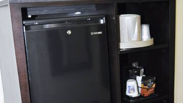 Un elegante minibar con frigorifero nero, forno a microonde e ripiano contenente una macchina da caffè, una lattina e un pacchetto di snack.