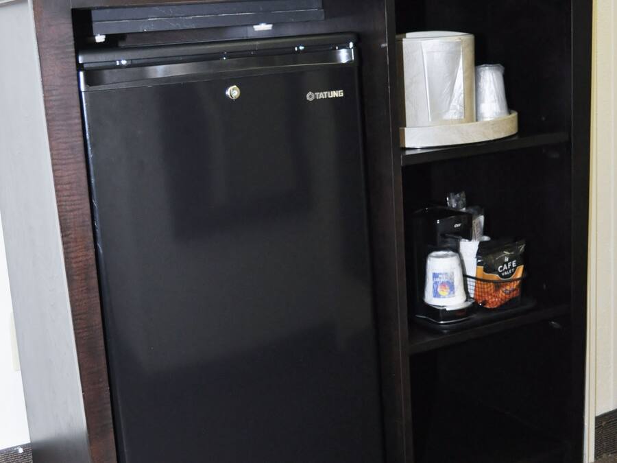 Un elegante minibar con frigorifero nero, forno a microonde e ripiano contenente una macchina da caffè, una lattina e un pacchetto di snack.