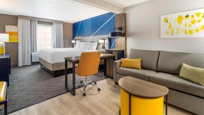 A hotel room with a bed, a desk, a chair, a sofa, and a small table.