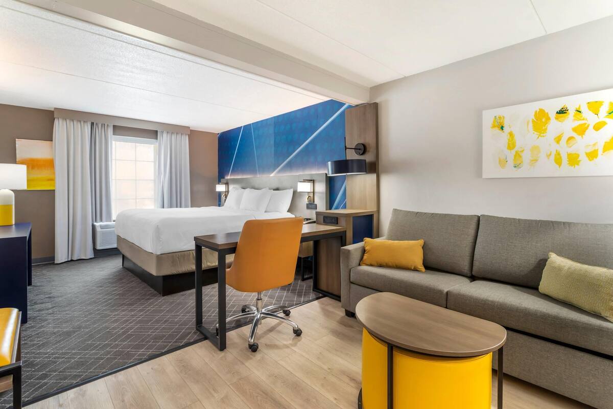 A hotel room with a bed, a desk, a chair, a sofa, and a small table.