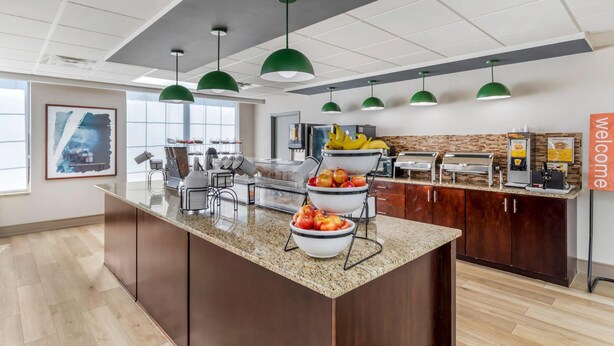 A modern kitchen area with granite countertops, green pendant lights, and a welcome sign.