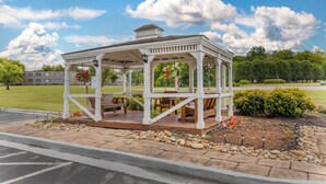 A gazebo with a roof and benches, surrounded by a landscaped garden with rocks and flowers.