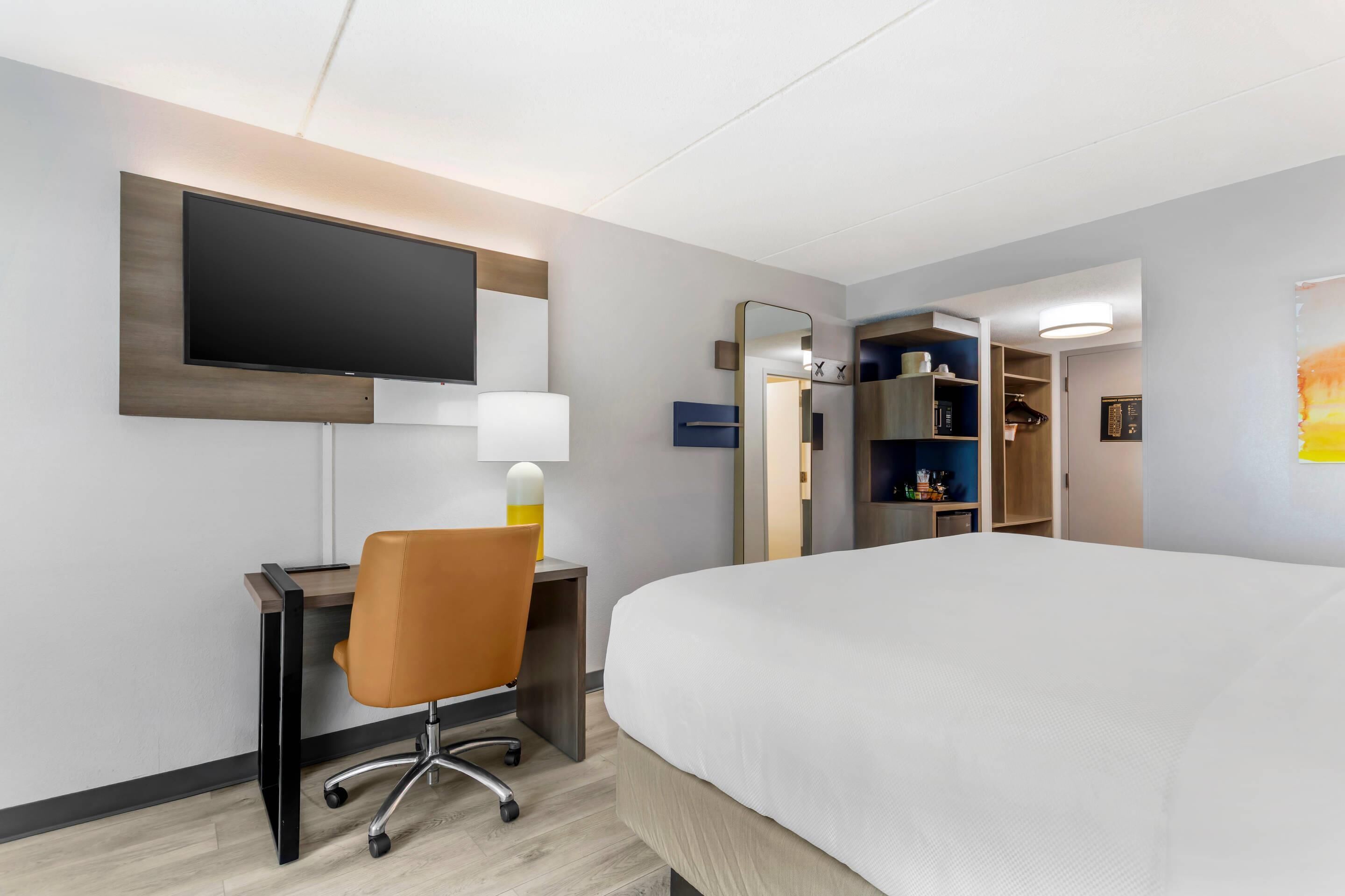 Ein Hotelzimmer mit Bett, Schreibtisch, Stuhl, Fernseher und begehbarem Kleiderschrank.
