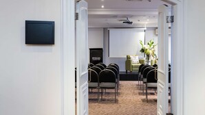 A conference room with a projector screen, a podium, and rows of chairs. - Rydges Camperdown (Camperdown)