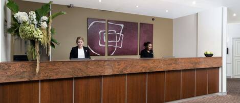 A reception desk with a large vase of flowers, two seated receptionists, and abstract wall art.