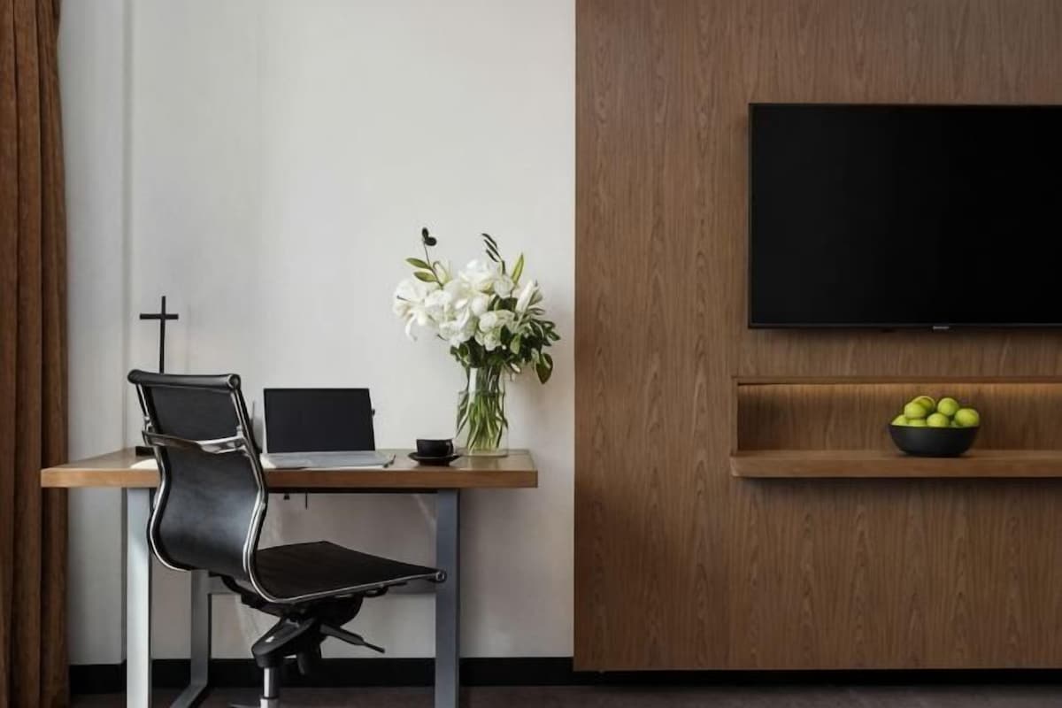 A modern room with a desk, chair, laptop, vase with flowers, and a TV on a wooden wall.