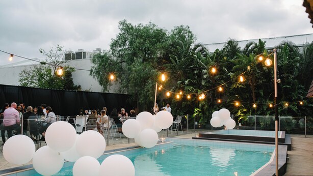 A pool area with white balloons and string lights, surrounded by greenery and a fence. - Rydges Camperdown (Camperdown)