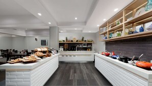 A modern kitchen area with a central island, a buffet setup, and a variety of kitchenware on shelves. - Rydges Camperdown (Camperdown)