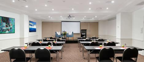 A conference room with tables, chairs, a projector screen, and a presentation screen.