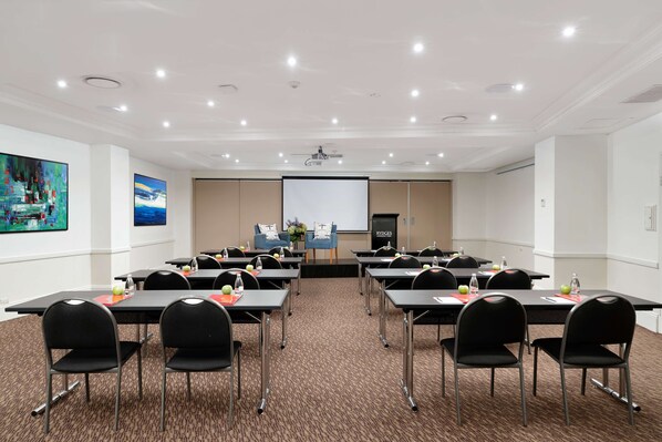 A conference room with tables, chairs, a projector screen, and a presentation screen. - Rydges Camperdown (Camperdown)