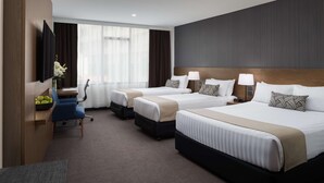 A hotel room with three beds, a desk, a chair, a TV, and a large window with curtains. - Rydges Camperdown (Camperdown)