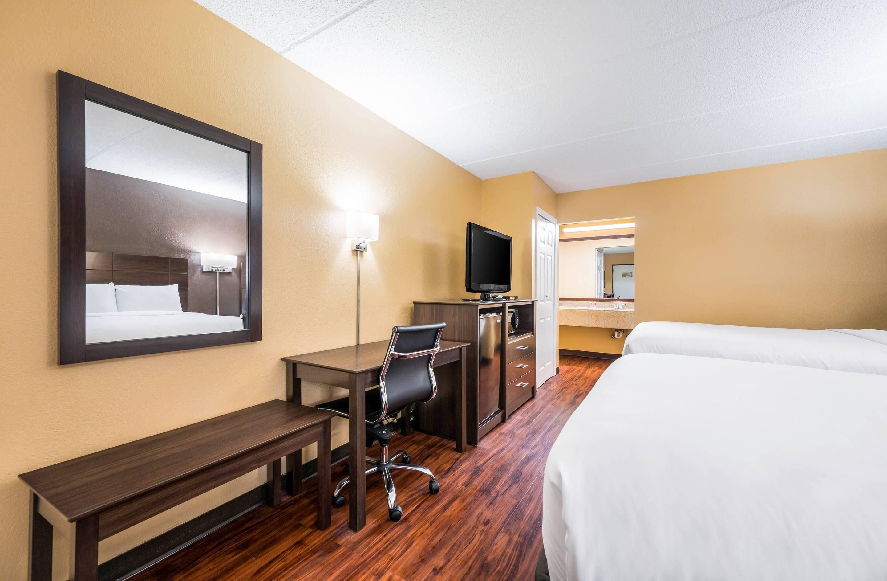Een hotelkamer met een bed, bureau, stoel, televisie en een spiegel.