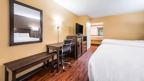 Habitación de hotel con cama, escritorio, silla, televisor y espejo.