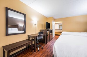 Ein Hotelzimmer mit Bett, Schreibtisch, Stuhl, Fernseher und Spiegel.