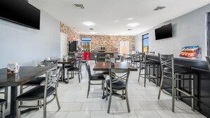 Un comedor moderno con varias mesas y sillas, una cocina al fondo y un televisor montado en la pared.