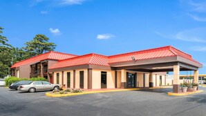 Un motel con techo rojo, zona de estacionamiento techada y aparcamiento con coches.
